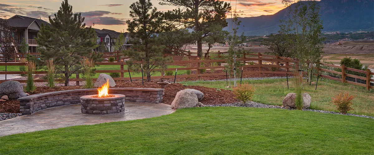 An outdoor space at dawn with a lit fireplace as hardscaping feature