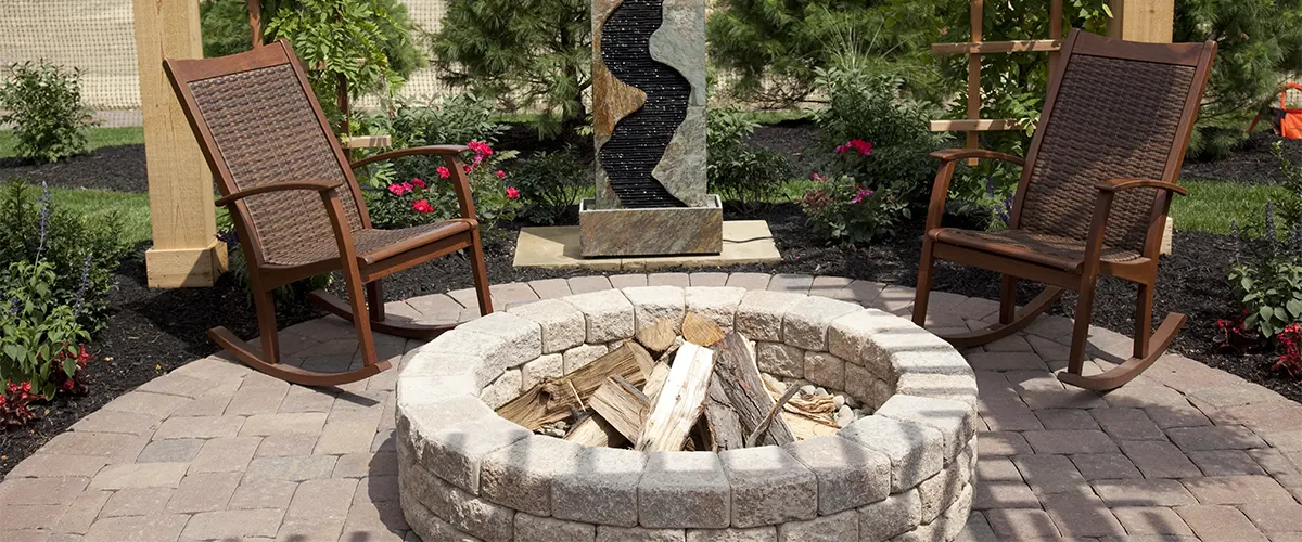 A brick fire pit with wood and two chairs