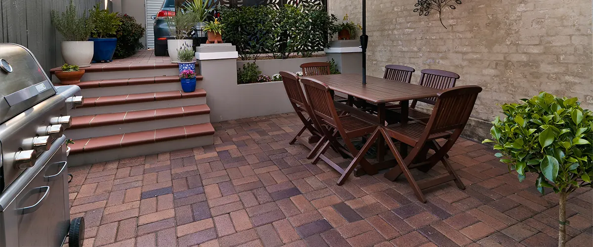 A beautiful weave basket brick patio with a barbecue and a wood table