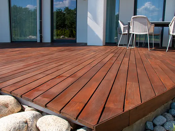 A wood deck with pebbles at its base and plastic chairs on it
