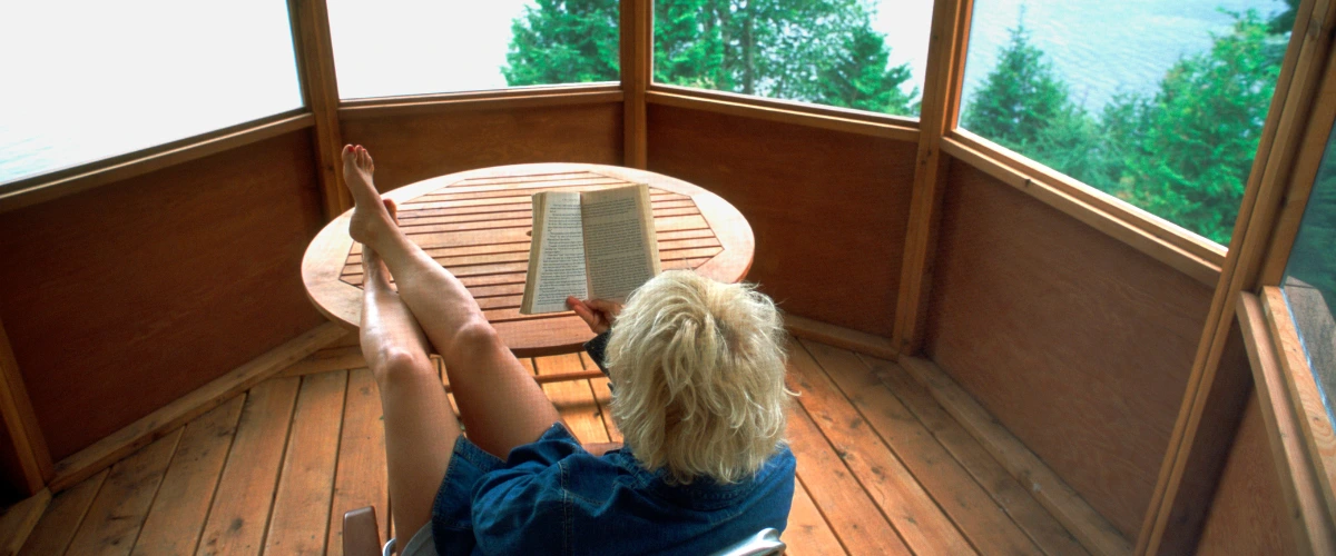 Woman reading a book in a wooden gazebo with lake and forest view, creating a cozy relaxation nook
