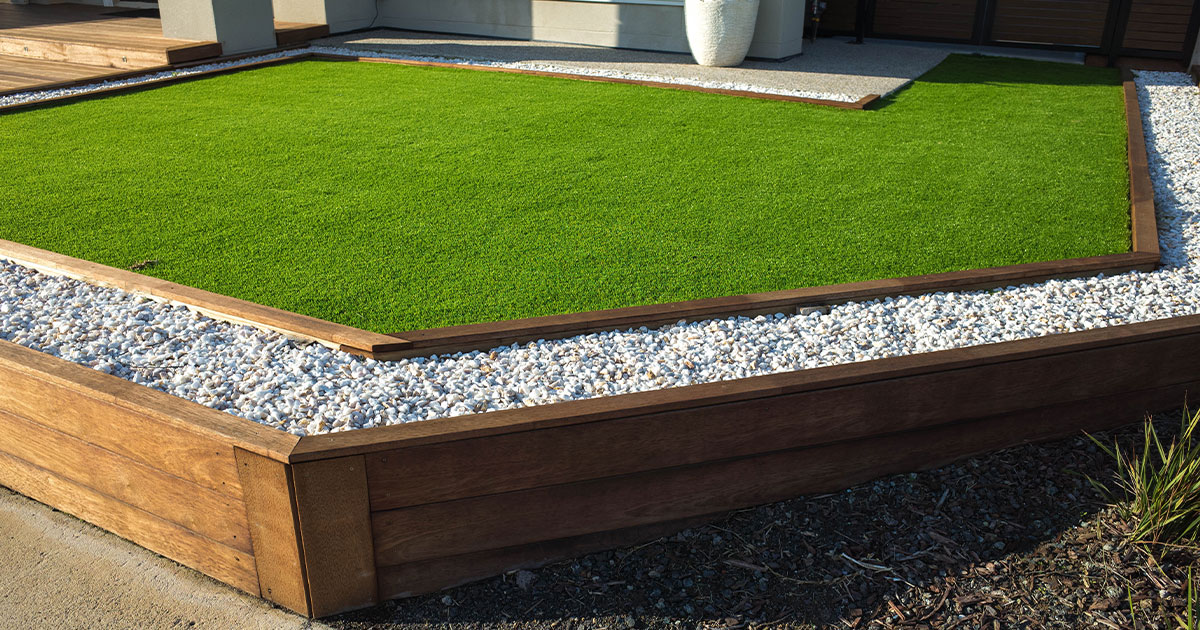 Lush green artificial turf installation in Denver backyard, bordered by pebbles and wooden beams.