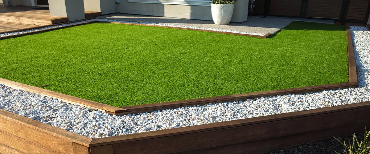 Lush green artificial turf installation in Denver backyard, bordered by pebbles and wooden beams.