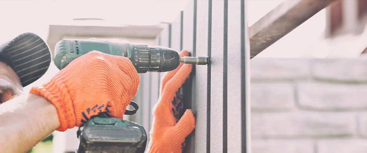 A worker wearing orange gloves and a cap using a drill for metal fence installation in a residential setting in Centennial.