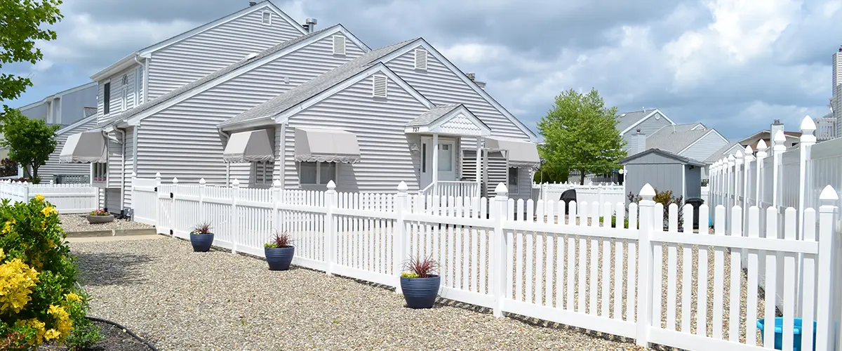 Charming neighborhood with white picket fences and modern grey houses, showcasing well-maintained yards and a peaceful residential setting.