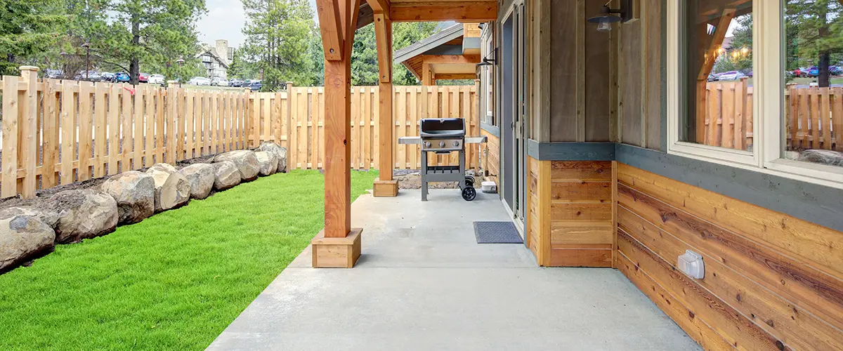 Small new back yard with wooden house and fence, fresh grass and BBQ on the concrete deck.