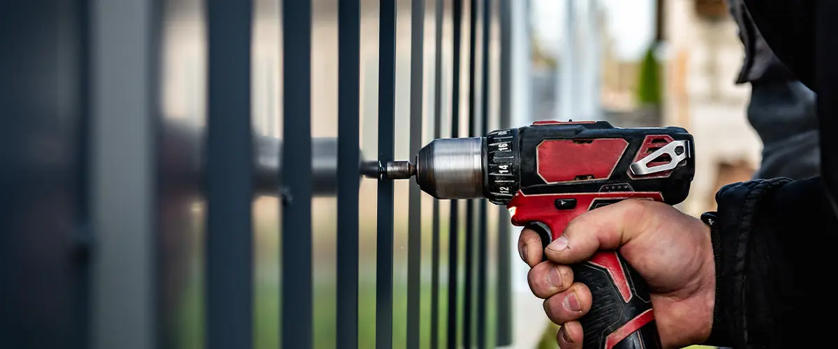 Worker installing metal fence using a power drill, showcasing durable and secure fencing solutions for fence installation in Englewood.