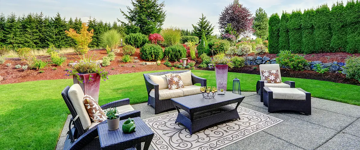 Beautifully landscaped backyard with a cozy outdoor seating area, lush green lawn, vibrant garden, and clear blue sky.