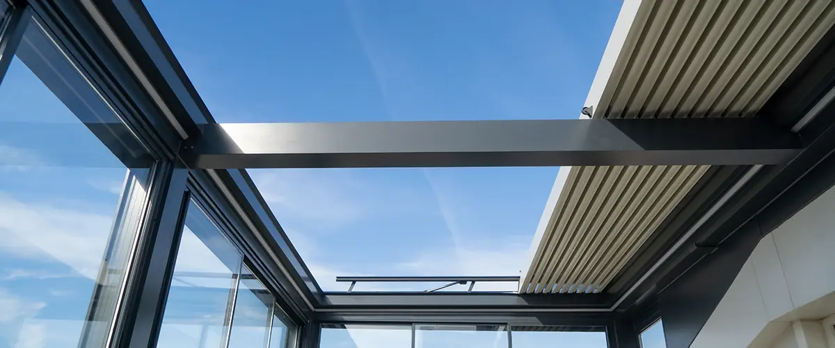 View of a motorized pergola frame with glass walls against a clear blue sky