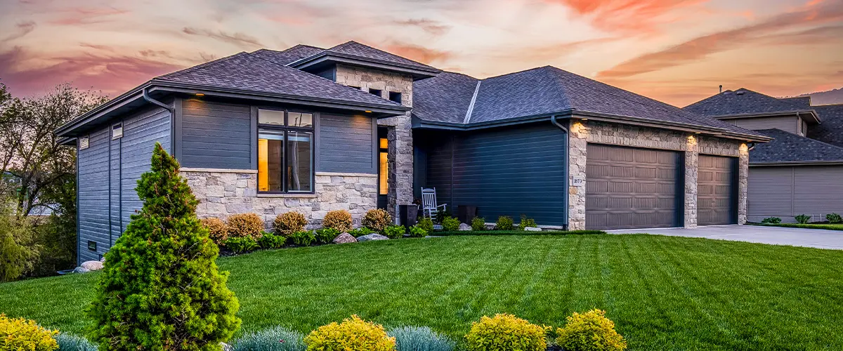 Modern home with dark siding, stone accents, a well-manicured lawn, and a vibrant sunset sky in the background.