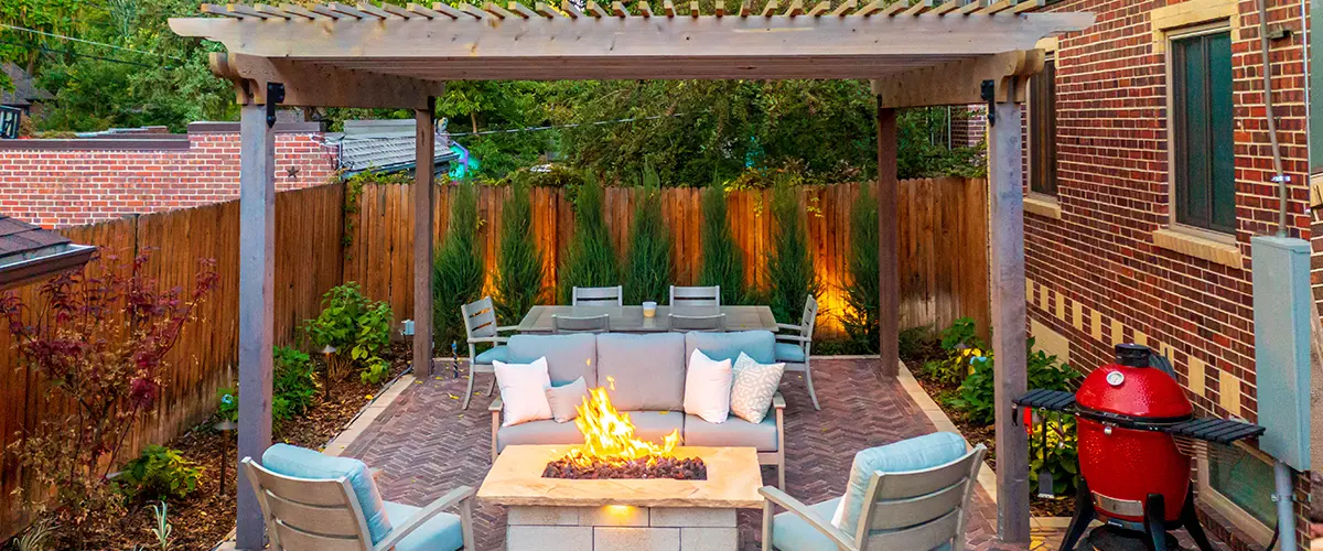 Evening view of a fire pit patio with seating and dining area under pergola lighting.