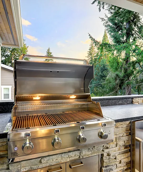 Professional stainless steel outdoor grill in Ken Caryl, set in stone veneer with granite countertops and a forest view.