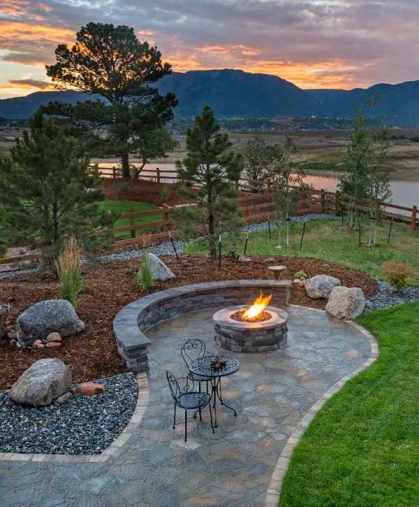 A cozy fire pit in a backyard with a scenic view of distant mountains under a clear blue sky.
