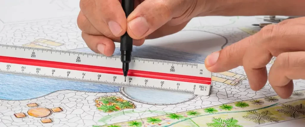 A person uses a ruler to sketch a detailed landscape design on paper.