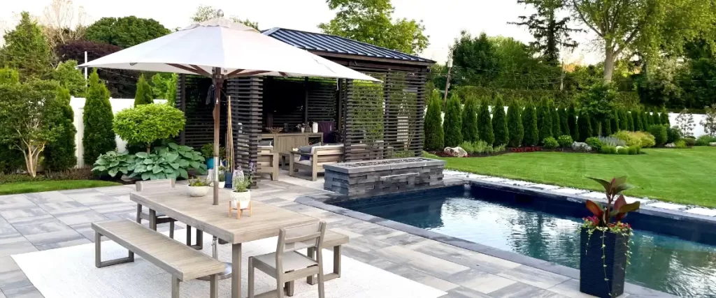 A paver patio, a swimming pool, and a slatted wooden structure in a backyard