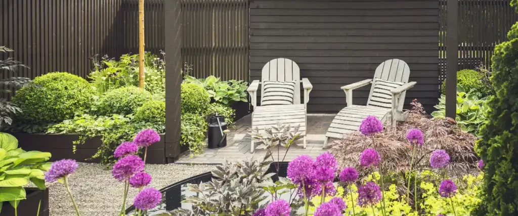 a contemporary garden patio area featuring a dark wooden fence, a seating area, and lush green and purple plantings