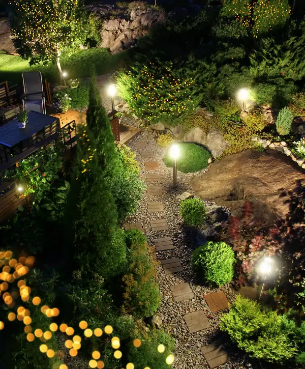 A beautifully lit stone pathway in a Wheat Ridge, CO backyard featuring warm landscape lighting, evergreen trees, and decorative string lights.